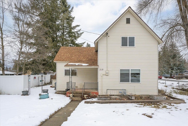 snow covered rear of property with roof with shingles, a vegetable garden, and fence