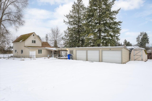 snow covered property featuring a garage, an outbuilding, and a storage unit