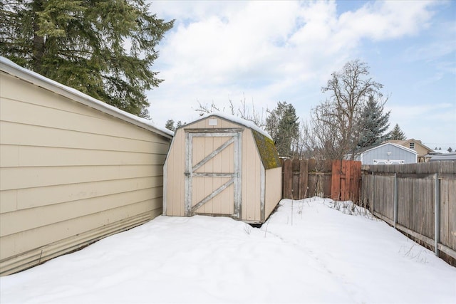 snow covered structure featuring a fenced backyard, an outdoor structure, and a storage shed