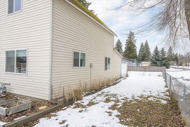 view of snowy exterior featuring fence and a garden