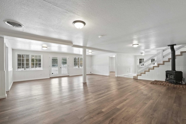 unfurnished living room featuring visible vents, dark wood-style flooring, a wood stove, a textured ceiling, and french doors