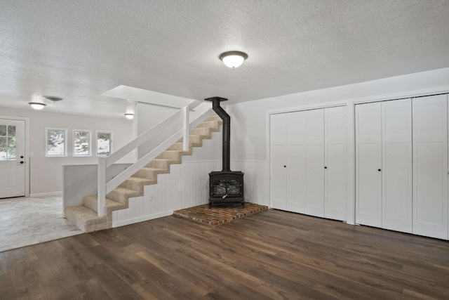 interior space with a textured ceiling, stairway, wood finished floors, and a wood stove