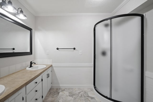 full bathroom with a wainscoted wall, crown molding, double vanity, a sink, and a shower stall