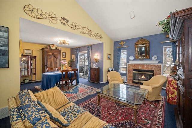 living area with a wealth of natural light, vaulted ceiling, dark colored carpet, and a premium fireplace