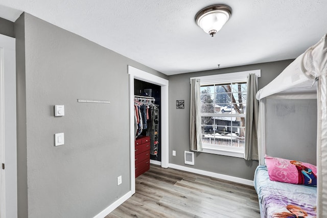 bedroom with a closet, a textured ceiling, baseboards, and wood finished floors