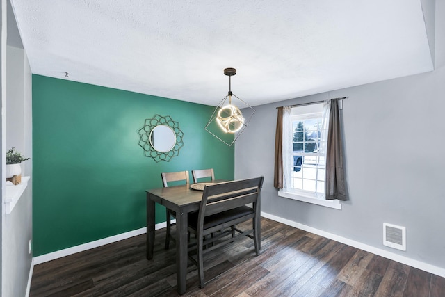 dining area with dark wood finished floors, visible vents, an accent wall, a textured ceiling, and baseboards