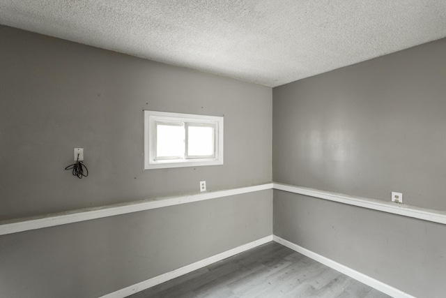 empty room with a textured ceiling, wood finished floors, and baseboards