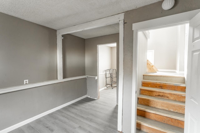 stairs with a textured ceiling, baseboards, and wood finished floors