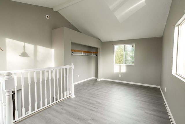 spare room with baseboards, lofted ceiling with beams, wood finished floors, and a healthy amount of sunlight