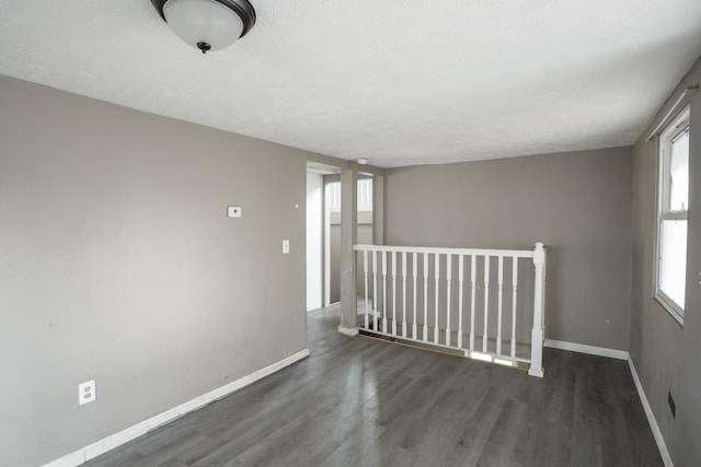 empty room with dark wood-type flooring, a textured ceiling, and baseboards