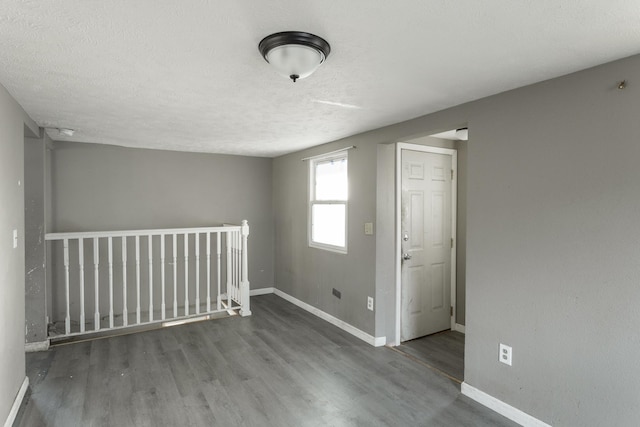 spare room with a textured ceiling, baseboards, and wood finished floors