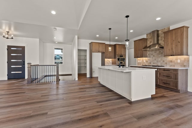 kitchen featuring hanging light fixtures, light countertops, a center island with sink, and wall chimney range hood