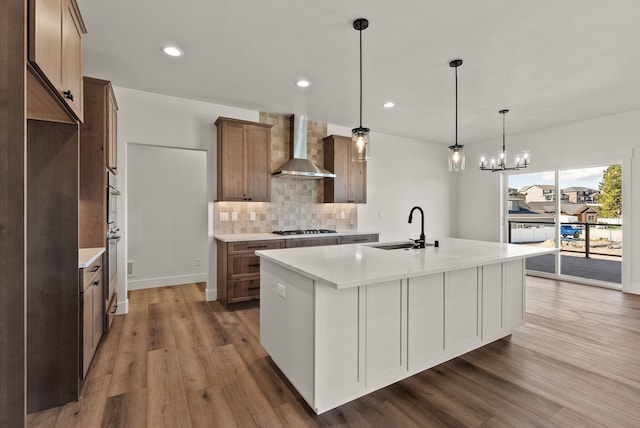 kitchen with light countertops, a center island with sink, a sink, and wall chimney exhaust hood