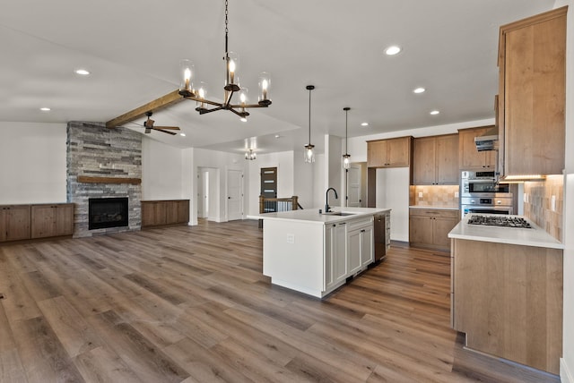 kitchen with lofted ceiling with beams, open floor plan, a kitchen island with sink, light countertops, and white cabinetry