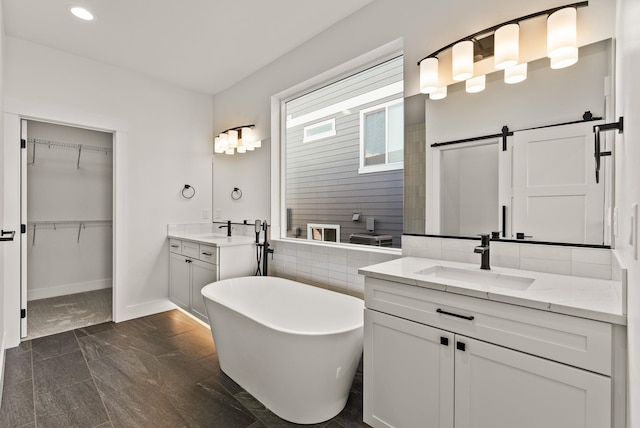 full bathroom featuring a spacious closet, two vanities, a soaking tub, and a sink