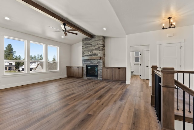 living room with vaulted ceiling with beams, a stone fireplace, wood finished floors, baseboards, and ceiling fan with notable chandelier