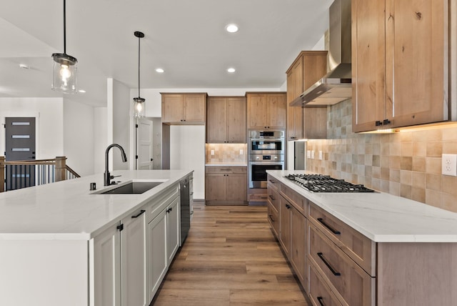 kitchen with a sink, wall chimney range hood, a large island, appliances with stainless steel finishes, and decorative light fixtures