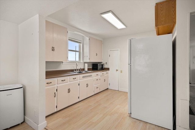 kitchen with light wood finished floors, stainless steel microwave, a sink, and freestanding refrigerator