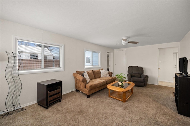 living area featuring baseboards, a ceiling fan, and light colored carpet