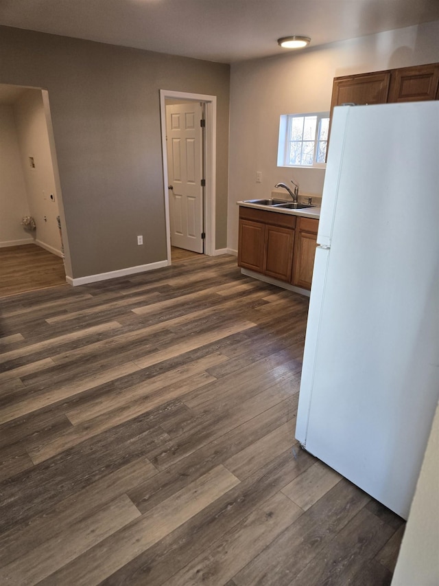 kitchen featuring brown cabinets, dark wood-style flooring, freestanding refrigerator, light countertops, and a sink