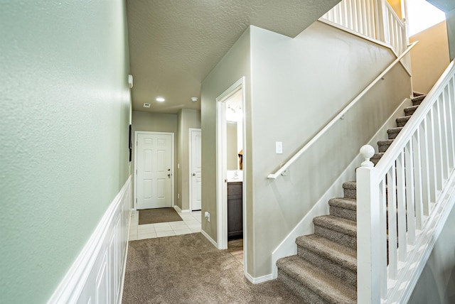 stairs featuring carpet floors, tile patterned flooring, a textured ceiling, and baseboards