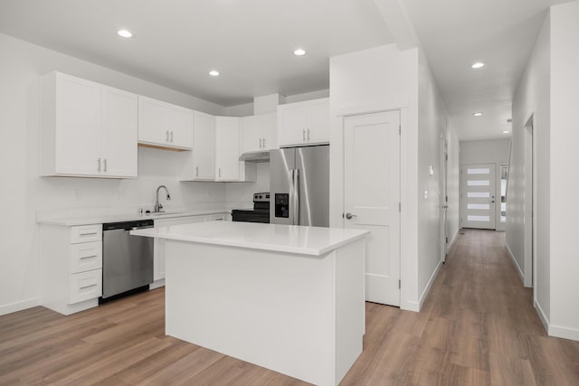 kitchen with a sink, a kitchen island, white cabinets, light countertops, and appliances with stainless steel finishes