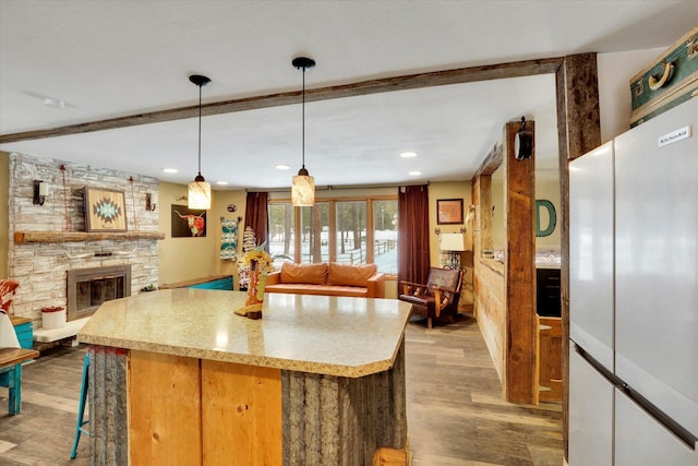 kitchen featuring pendant lighting, light countertops, open floor plan, a stone fireplace, and light wood-type flooring