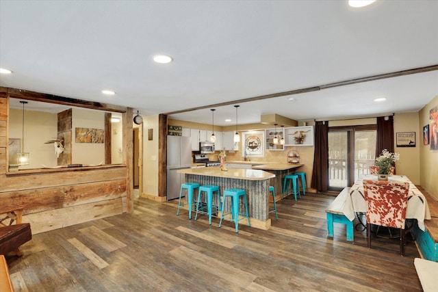 kitchen featuring dark wood-style floors, decorative light fixtures, stainless steel appliances, light countertops, and a kitchen breakfast bar