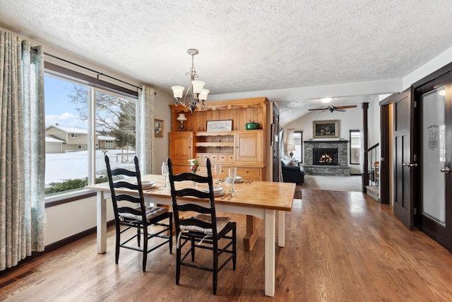 dining room featuring visible vents, a stone fireplace, a textured ceiling, wood finished floors, and ceiling fan with notable chandelier