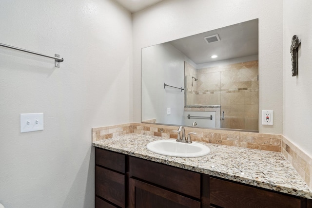 full bath featuring tiled shower, vanity, and visible vents