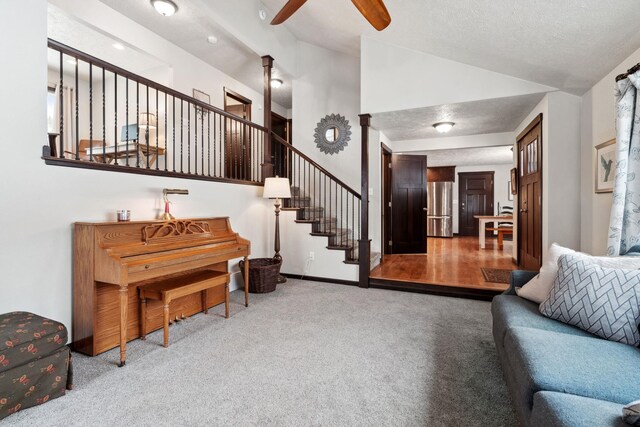 living room with a textured ceiling, a ceiling fan, stairway, carpet flooring, and lofted ceiling