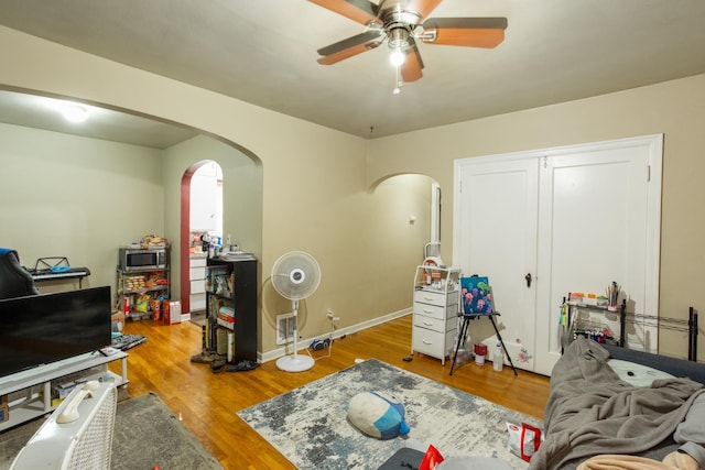 interior space featuring arched walkways, ceiling fan, wood finished floors, and baseboards