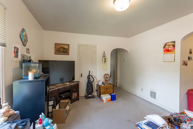 living area with visible vents, arched walkways, and light colored carpet