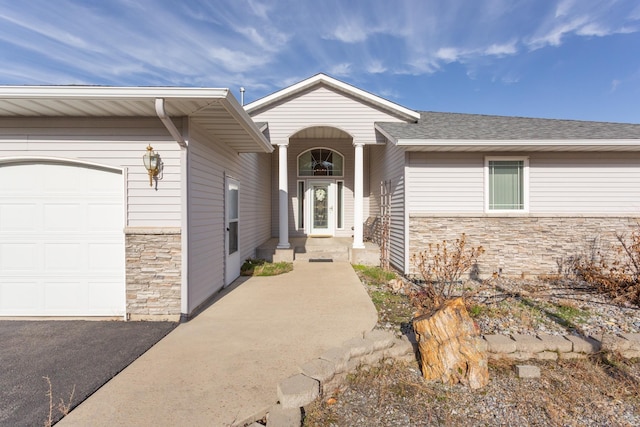 view of exterior entry featuring a garage, stone siding, and roof with shingles