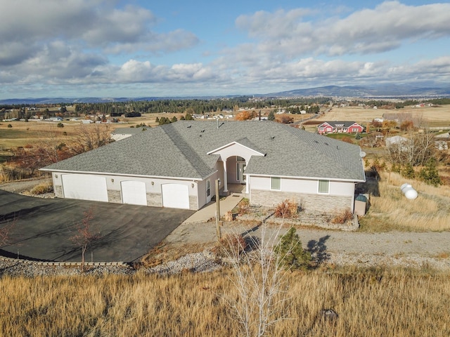 view of front of house featuring a shingled roof, stone siding, aphalt driveway, an attached garage, and a mountain view