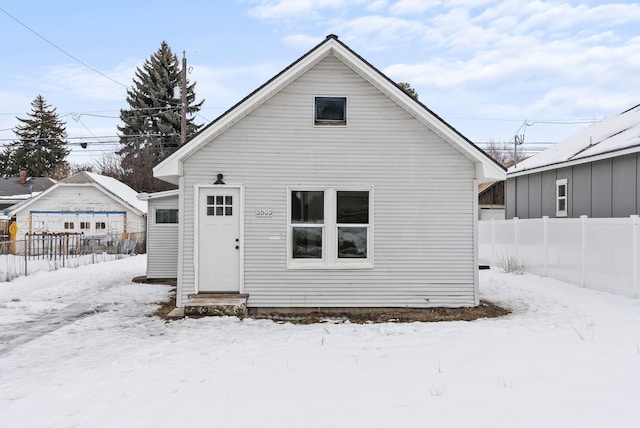 snow covered back of property featuring entry steps and fence