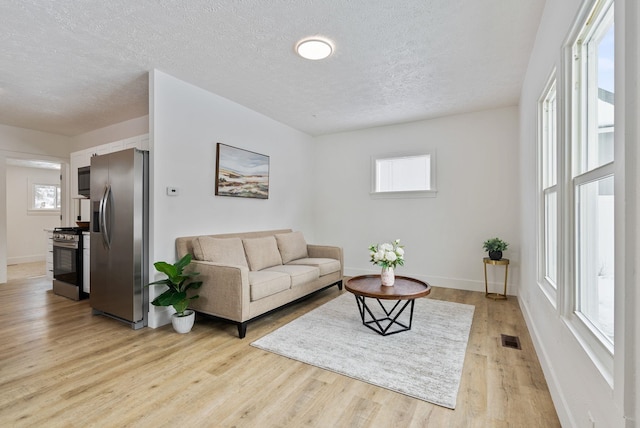 living room with a wealth of natural light, light wood-type flooring, visible vents, and baseboards