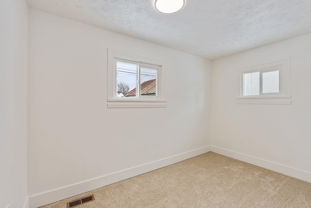 spare room featuring visible vents, plenty of natural light, light carpet, and baseboards