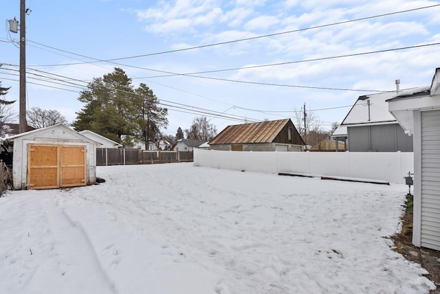 snowy yard with a garage, a storage shed, a fenced backyard, and an outdoor structure