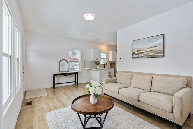 living area featuring visible vents, light wood-style flooring, baseboards, and a textured ceiling