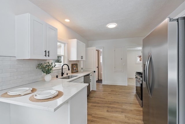 kitchen with appliances with stainless steel finishes, white cabinetry, a sink, light stone countertops, and a peninsula