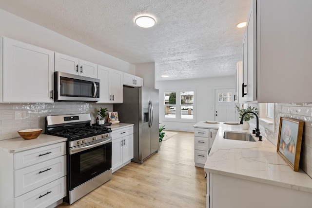 kitchen featuring appliances with stainless steel finishes, white cabinetry, a sink, and light stone countertops