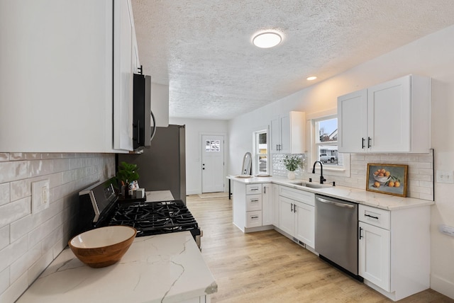 kitchen featuring appliances with stainless steel finishes, white cabinets, a sink, and light stone counters