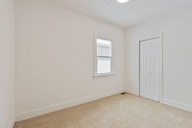 spare room with a textured ceiling, baseboards, visible vents, and light colored carpet