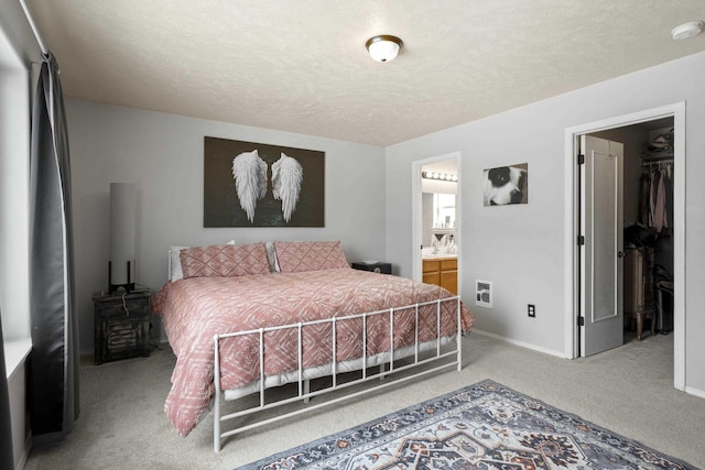 bedroom with light carpet, baseboards, ensuite bath, a walk in closet, and a textured ceiling