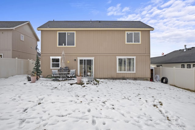 snow covered back of property with a fenced backyard