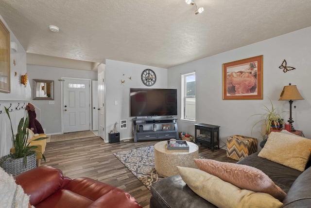 living room featuring a wood stove, a textured ceiling, baseboards, and wood finished floors