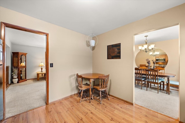 dining area featuring baseboards, a notable chandelier, light carpet, and light wood finished floors