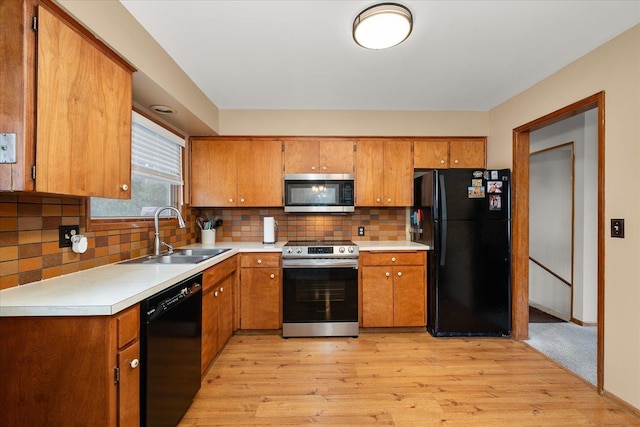 kitchen with brown cabinets, a sink, light countertops, black appliances, and backsplash