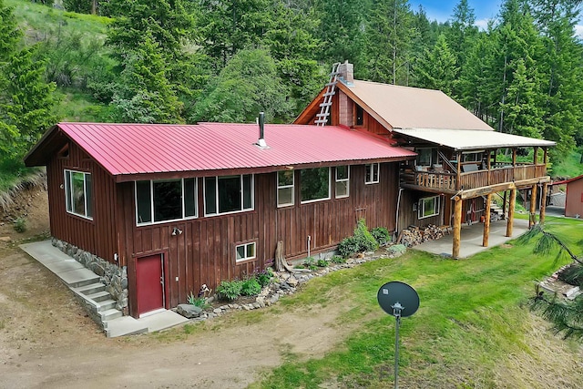 exterior space featuring a wooden deck, a patio, a chimney, metal roof, and a yard